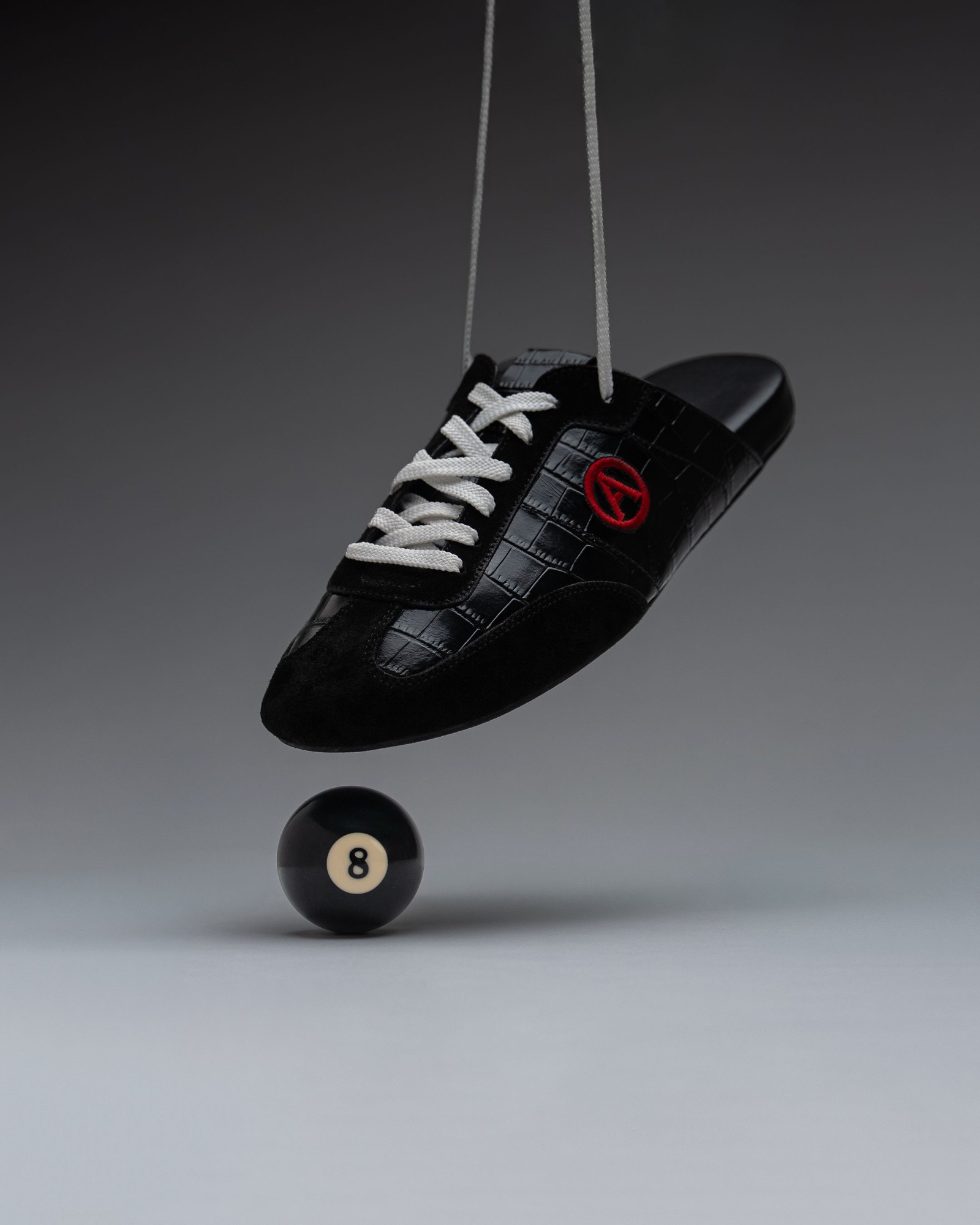 Eko Goose black slide suspended by its laces above an eight ball