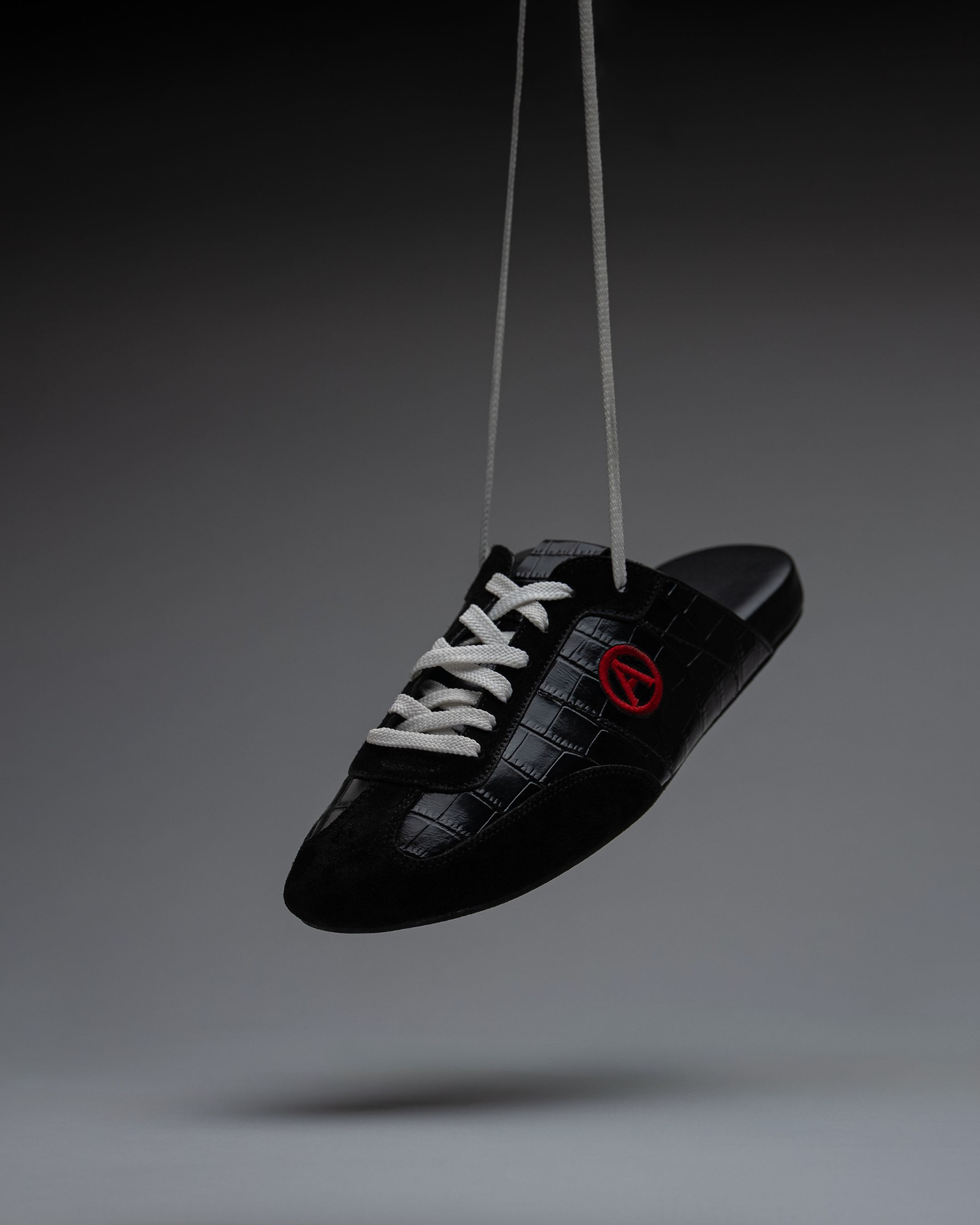 Eko Goose black slide hanging from white laces on a grey backdrop